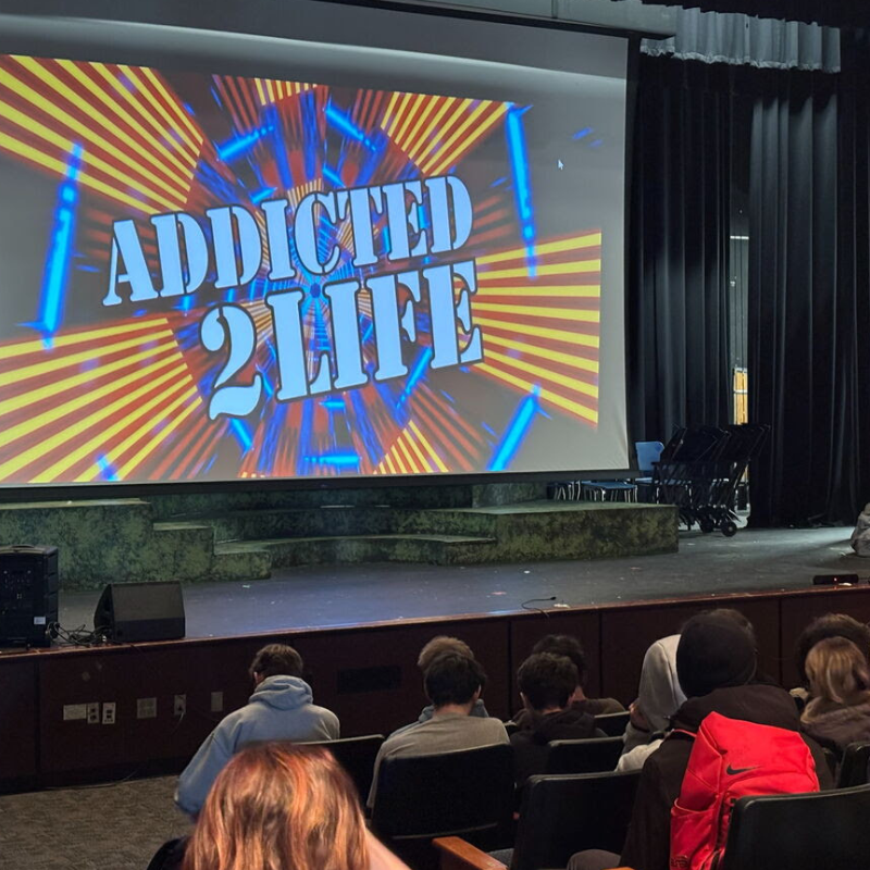 A large screen displays "ADDICTED 2 LIFE" with a vibrant, radial background.