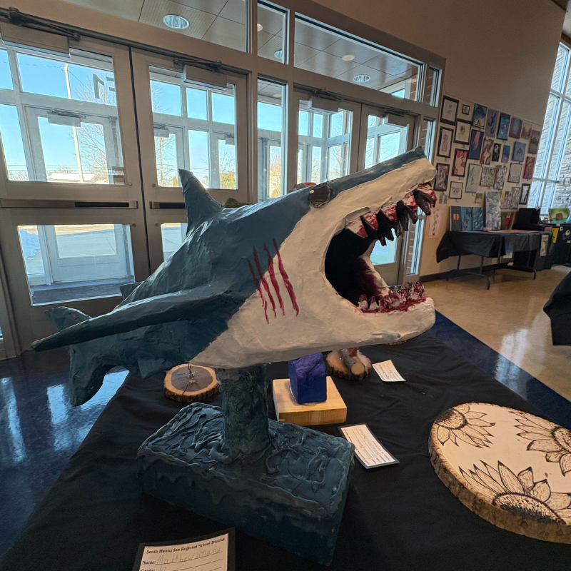 A detailed sculpture of a shark with its mouth open, displayed at an art exhibition.
