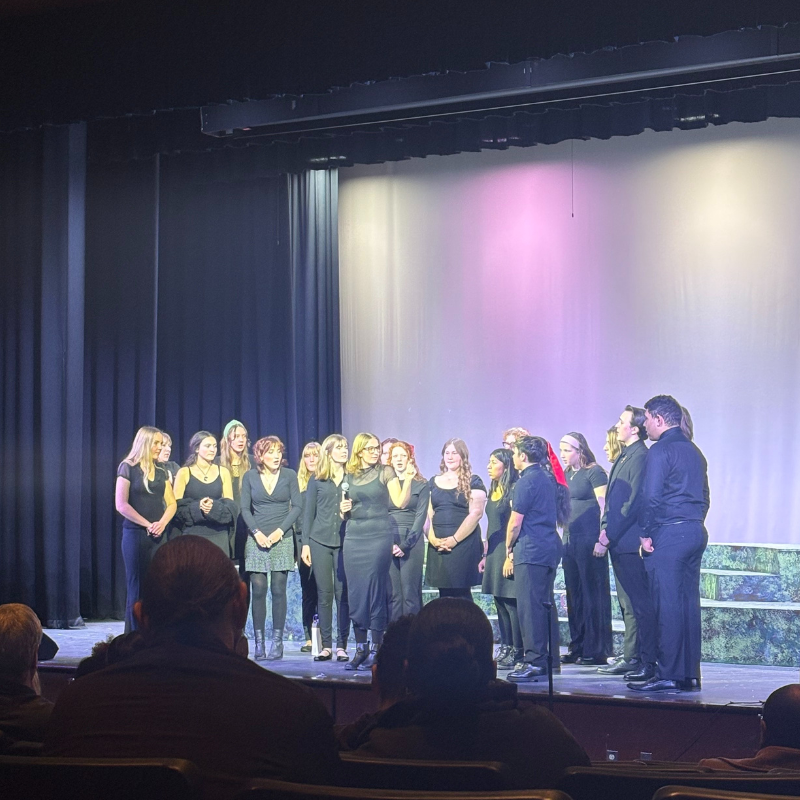 A group of people in black attire stand on a stage in front of a lit backdrop.