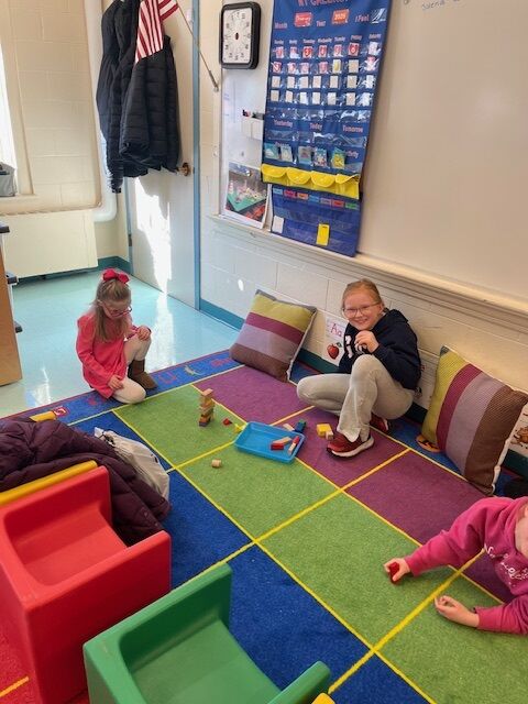 Children play with building blocks on a colorful classroom rug.