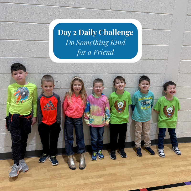 Seven children stand in a line against a white brick wall, with a blue banner above them reading 'Day 2 Daily Challenge: Do Something Kind for a Friend'.