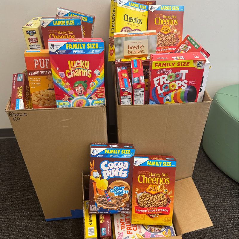 Several cardboard boxes are filled with a variety of cereal boxes, including Lucky Charms, Froot Loops, and Cheerios.