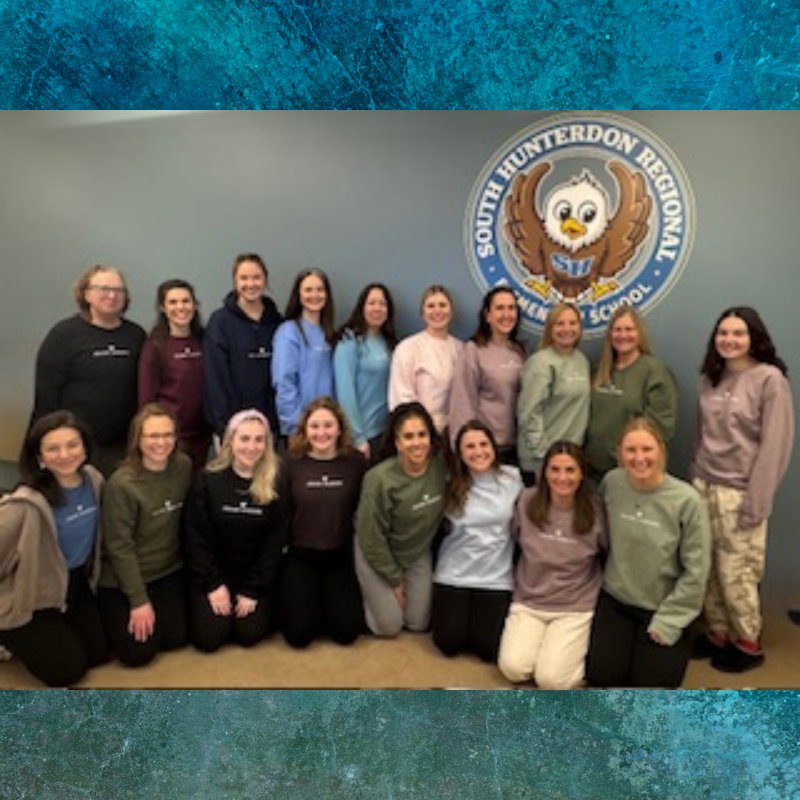 A group of women stand and kneel in front of a school logo.