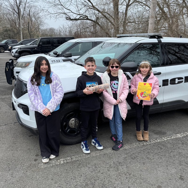 Four children stand in front of a police car, holding a box of donuts and a thank you sign.