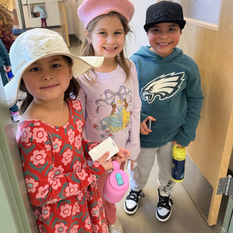 Three children stand together, two girls in hats and a boy in a baseball cap.