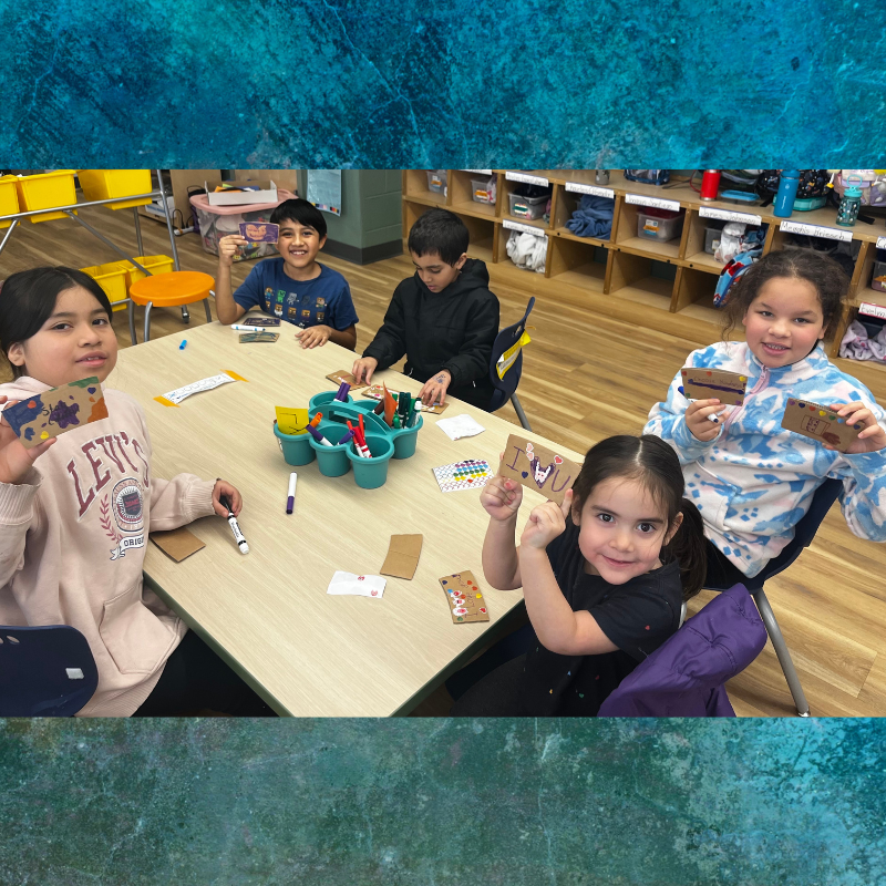 Children proudly display handmade cards they created at a classroom art table.