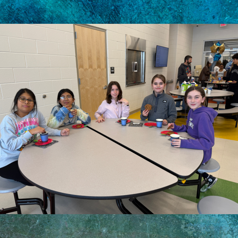 Five young girls sit at a round table, holding cups and snacks.