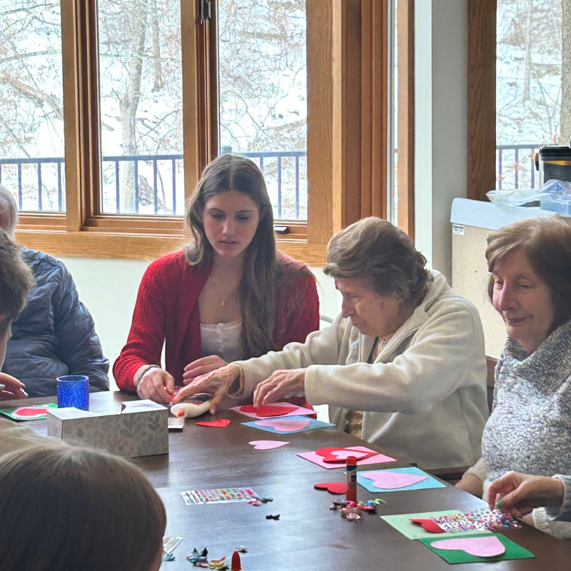 People of different ages are crafting heart-shaped cards at a table.