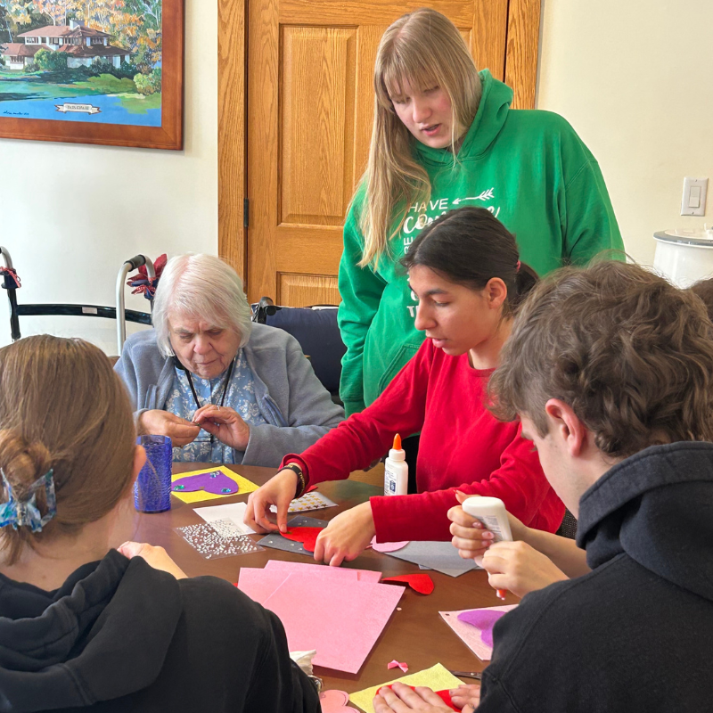 A group of people of different ages are crafting together at a table, with colorful paper and glue visible.