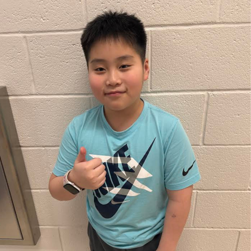 A young boy in a blue Nike t-shirt gives a thumbs-up gesture.