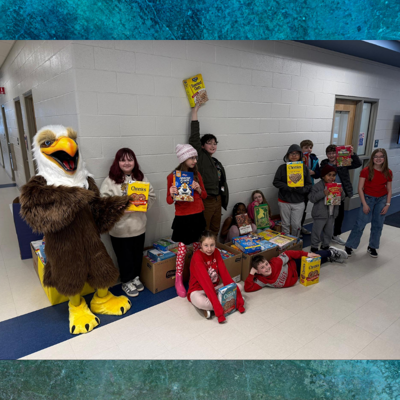 A group of children and an eagle mascot stand around boxes of cereal in a school hallway.