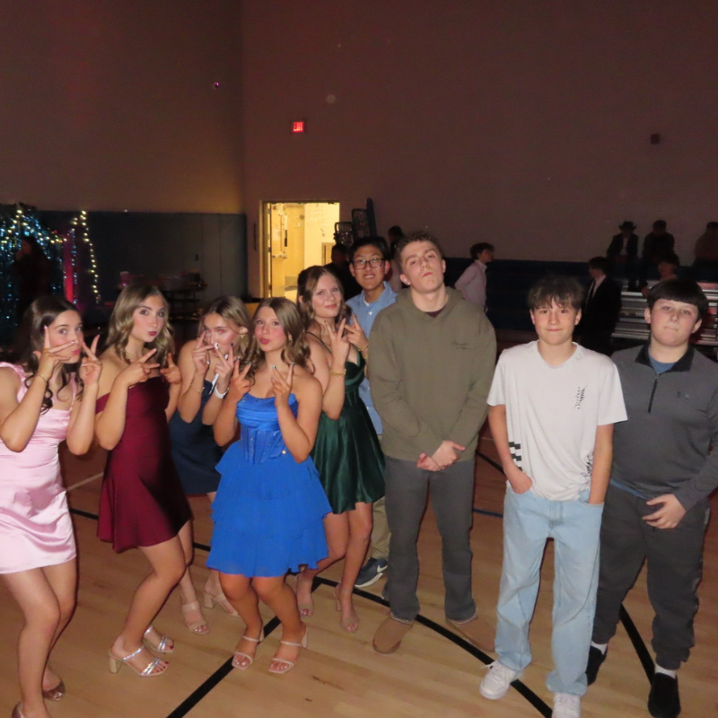 A group of teenagers in formal attire pose for a photo in a gymnasium.