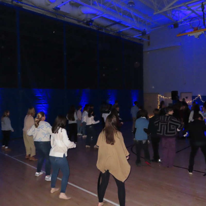 A group of people dance in a gymnasium illuminated by blue lights.