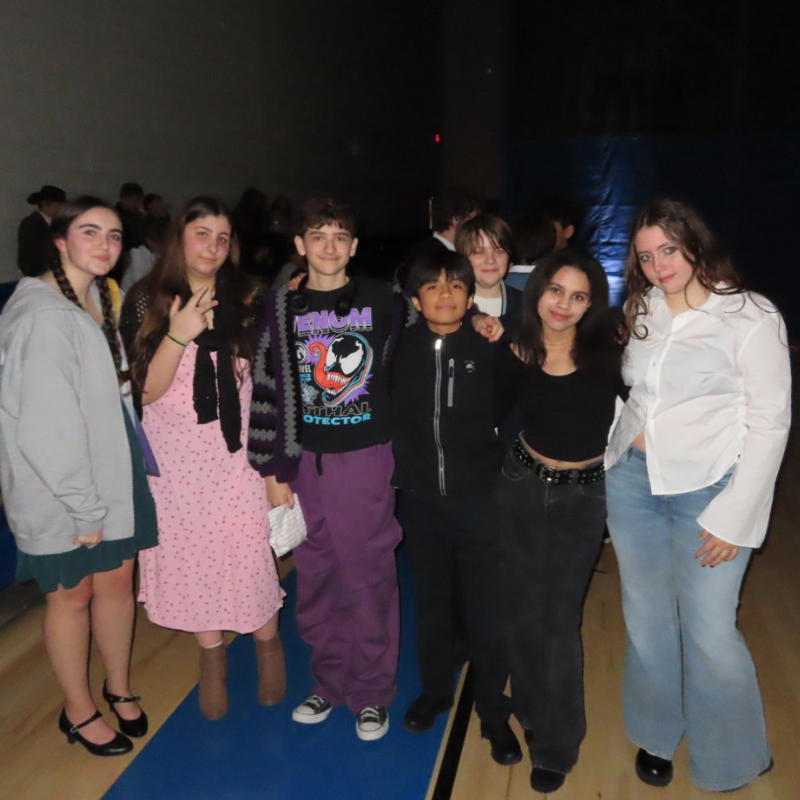 A group of seven young people stand together, posing for a photo indoors.