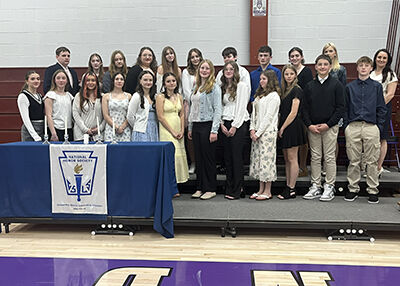A group of students stands together for a photo, some in formal attire, in front of a table with a National Honor Society banner.