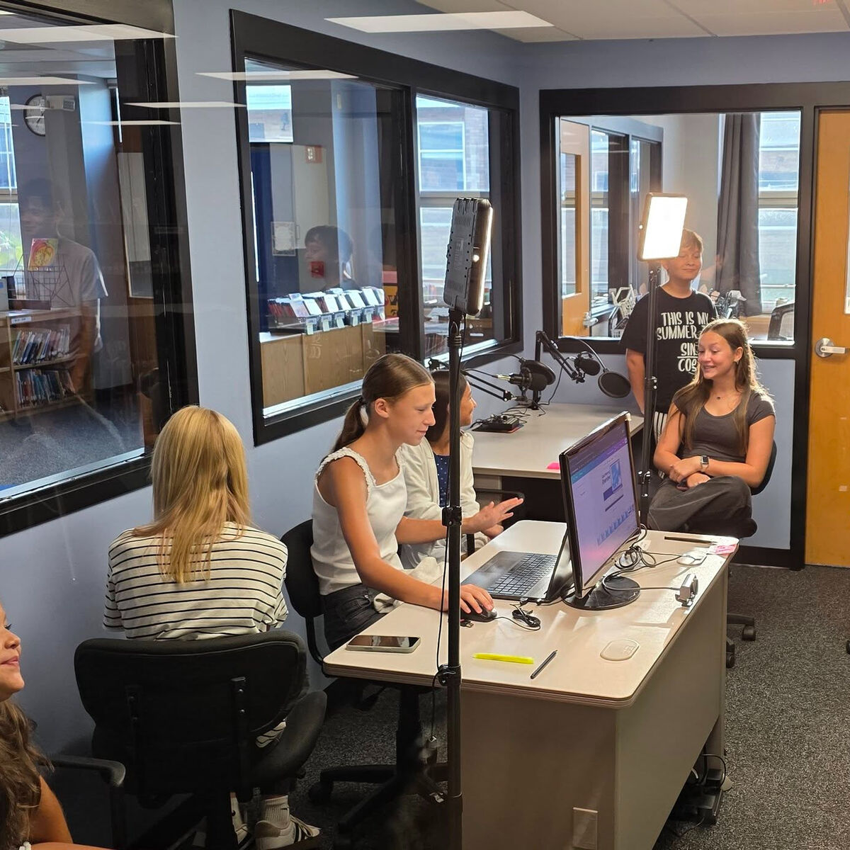 A group of students works in a media production room with recording equipment and computers.