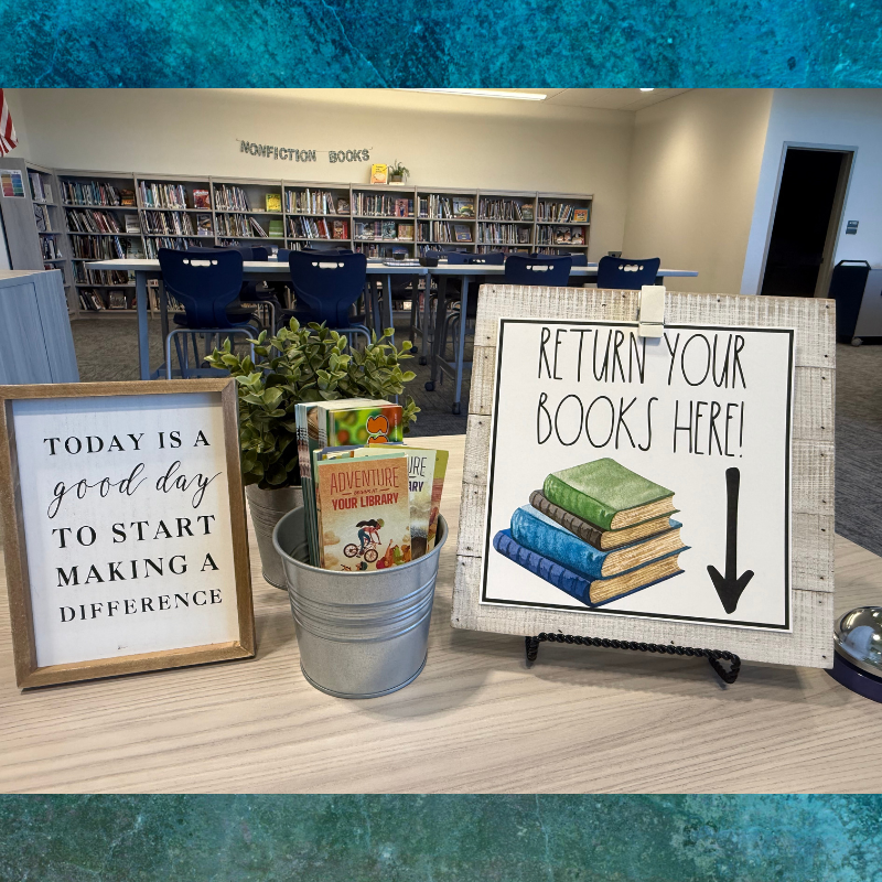 A library display features a sign reading 'RETURN YOUR BOOKS HERE!' with an illustration of stacked books.