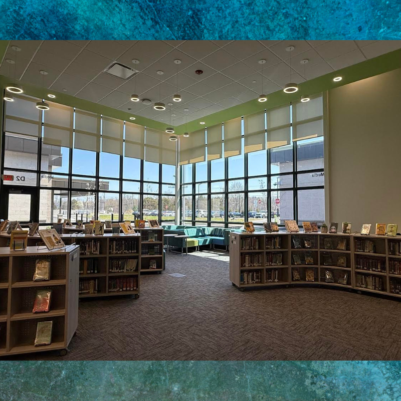 A modern library interior with floor-to-ceiling windows, bookshelves, and comfortable seating areas.