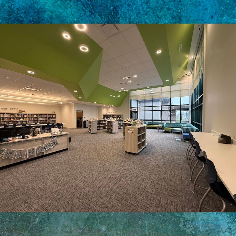 A modern library interior with colorful green ceiling accents and rows of bookshelves.