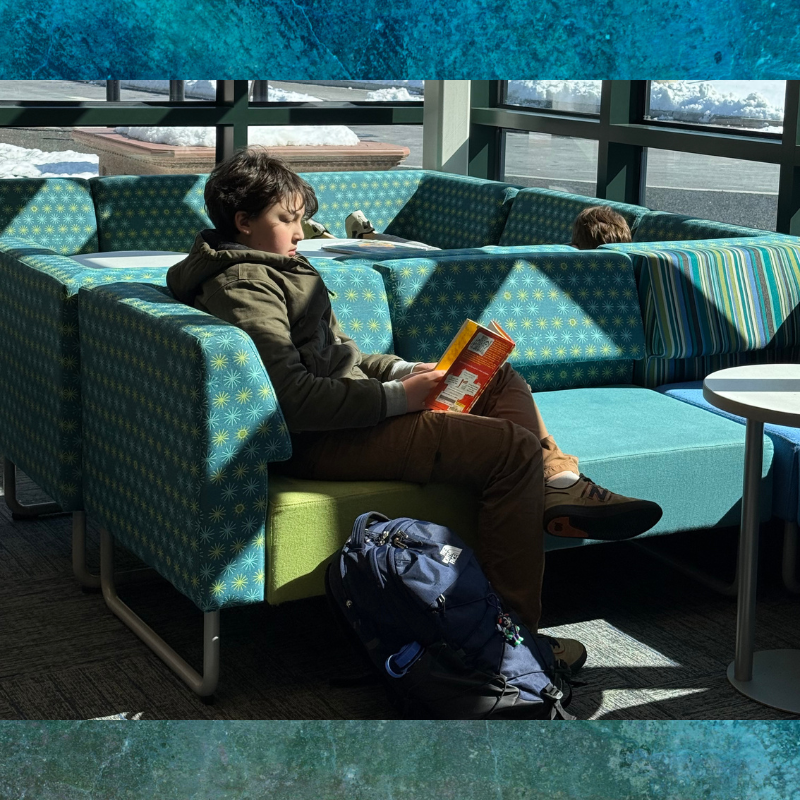 A young person sits on a colorful sectional sofa, engrossed in reading a book.