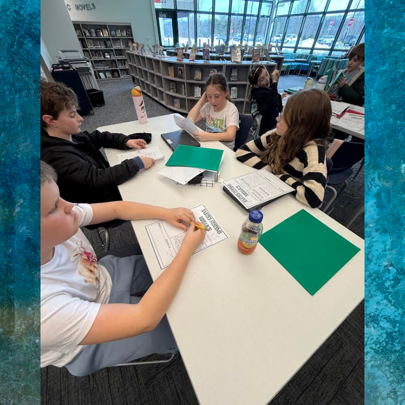 Students collaborate around a white table in a library, working on assignments.