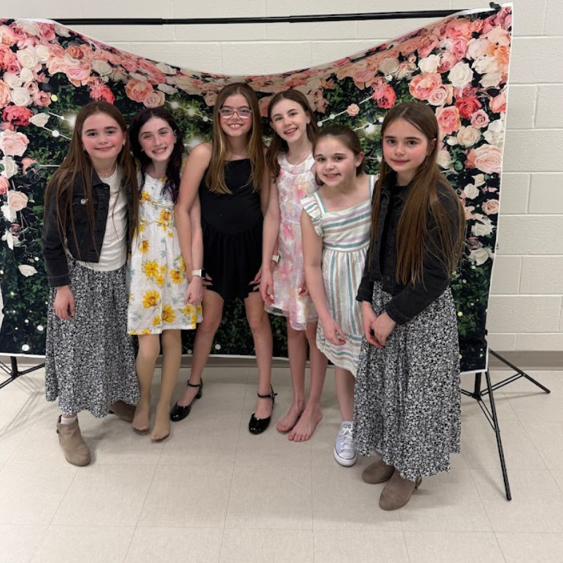 Six young girls pose for a photo in front of a floral backdrop.