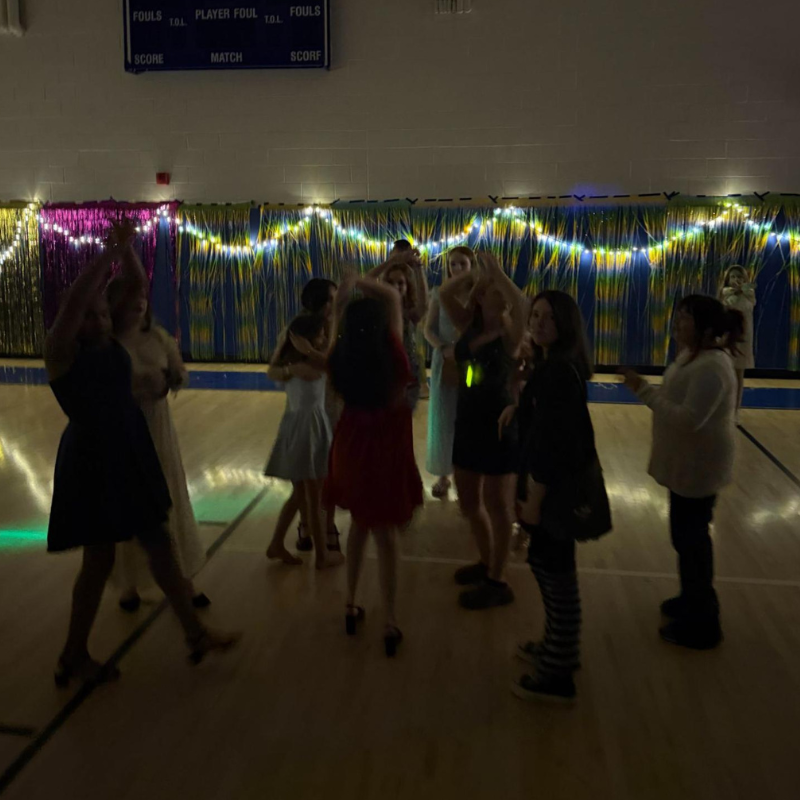 A group of young people dance in a gymnasium decorated with streamers and lights.