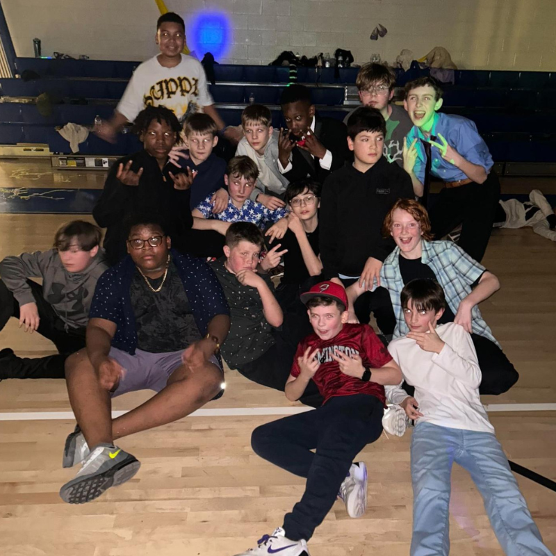 A group of young boys pose for a photo on a wooden floor, some sitting and some standing.