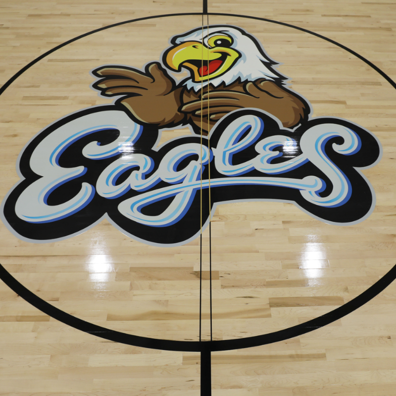 A cartoon eagle mascot with the word "Eagles" is painted on a polished wooden basketball court.