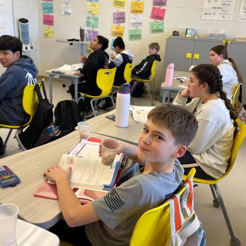 Students sit at desks in a classroom, with one boy smiling at the camera.
