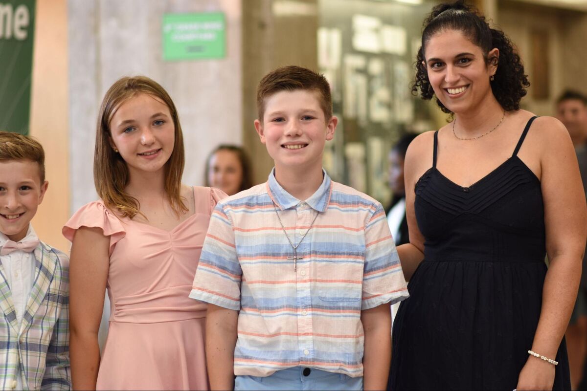 Three children and a woman smile for a photo indoors.