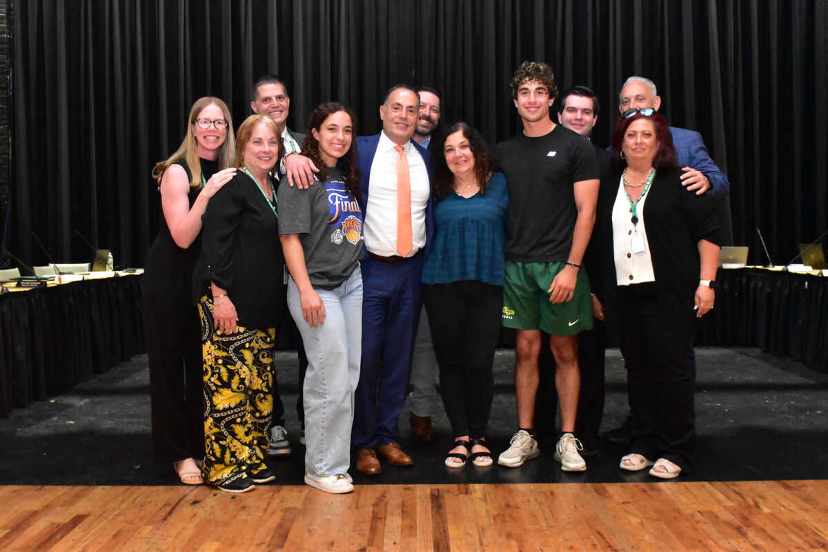 A diverse group of people pose for a photo in front of a black curtain.