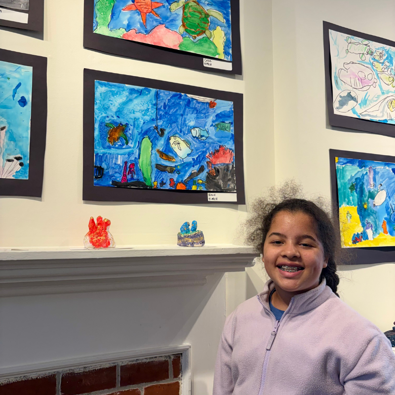 A young girl smiles in front of a wall displaying colorful underwater-themed artwork.