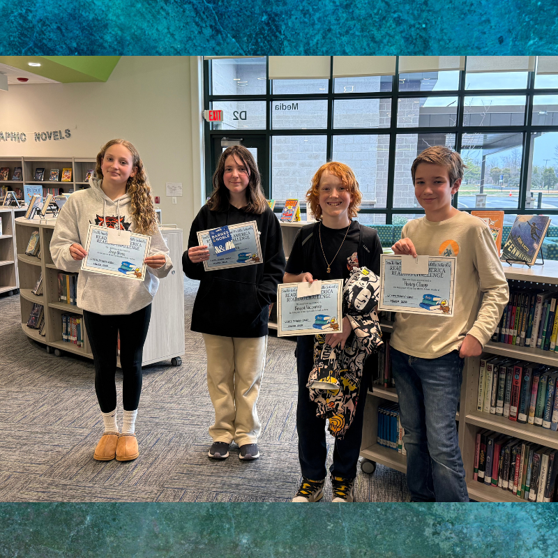 Four young people stand in a library, holding certificates for a reading challenge.