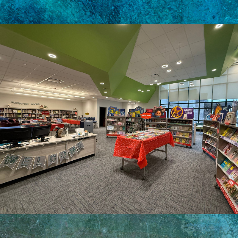 A brightly lit library with shelves of books, display tables, and a welcome banner.