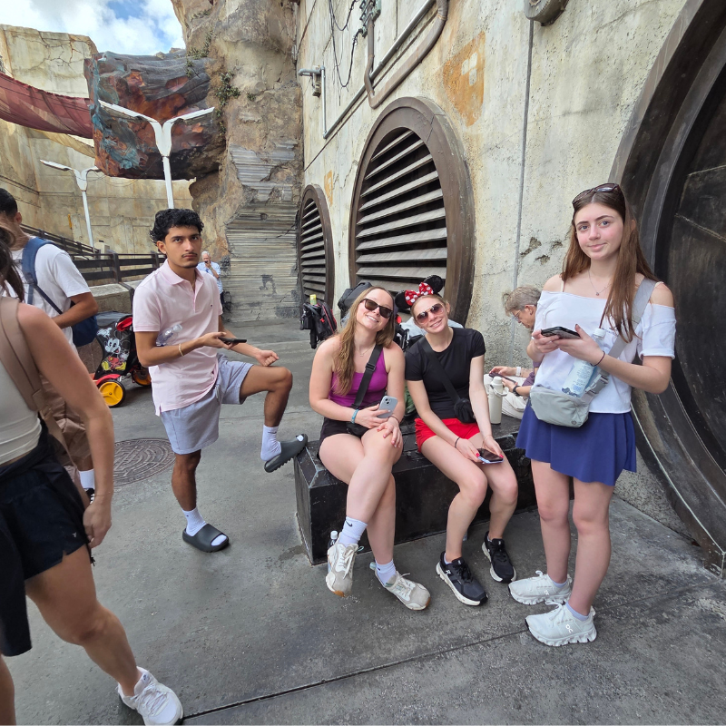 A group of young people are gathered in an outdoor area with themed architecture.