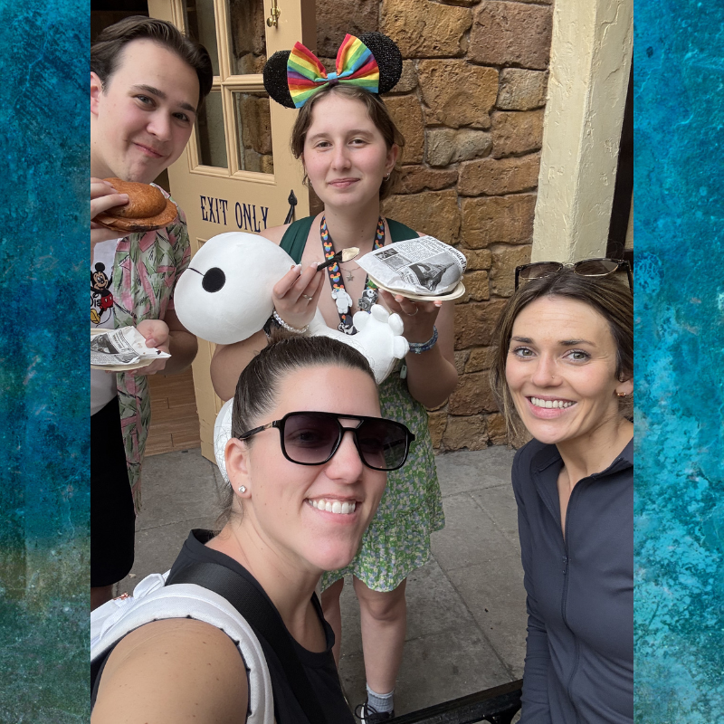 Four smiling people pose for a photo, holding food and a Baymax plush toy.
