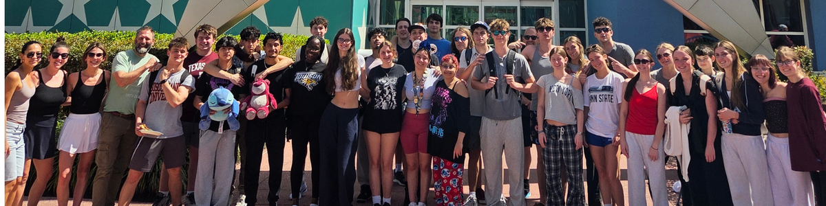A diverse group of young adults and a few adults pose for a photo in front of a building with large star designs.