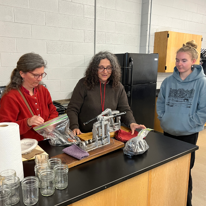 Three people stand around a counter in a room, with a mechanical device in the center.
