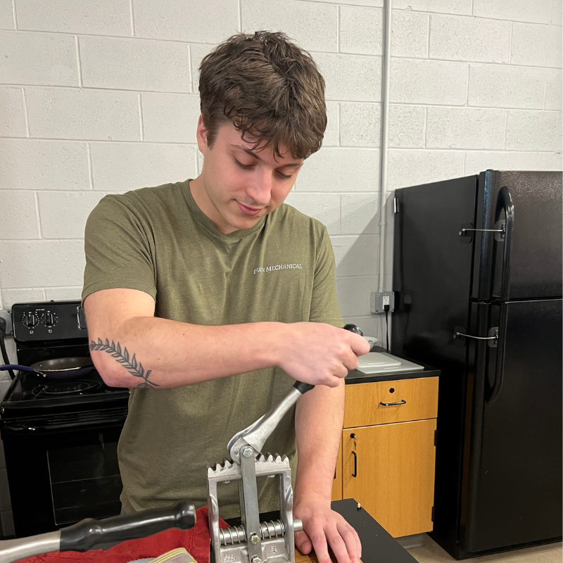 A young man in a green t-shirt with 'DUR MECHANICAL' printed on it operates a metal tool.