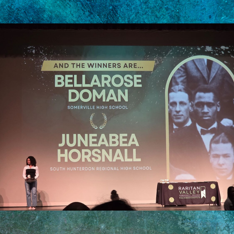 A young woman stands on a stage holding an award, with names of winners displayed on a large screen behind her.
