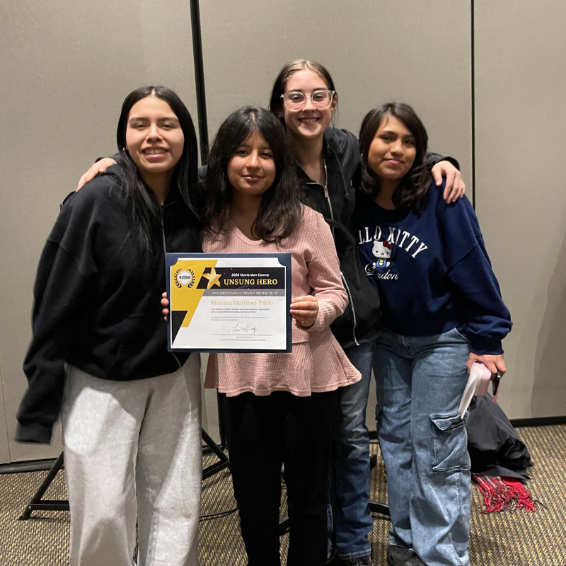 Four young women smile as one holds a certificate for "UNSUNG HERO" from 2026 Hunterdon County.