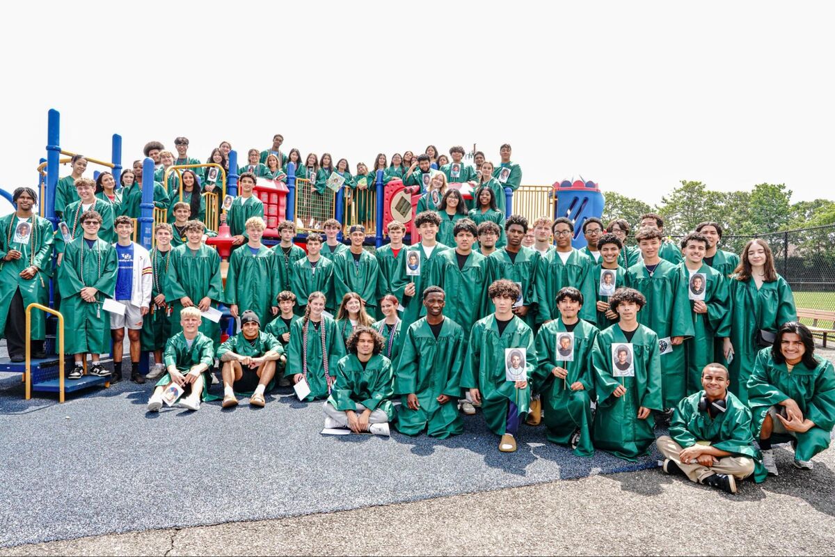 A large group of graduates in green gowns pose for a photo on a playground.