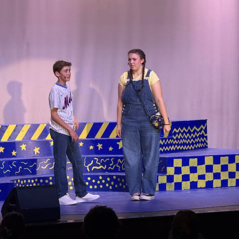Two young performers stand on a brightly decorated stage during a play.