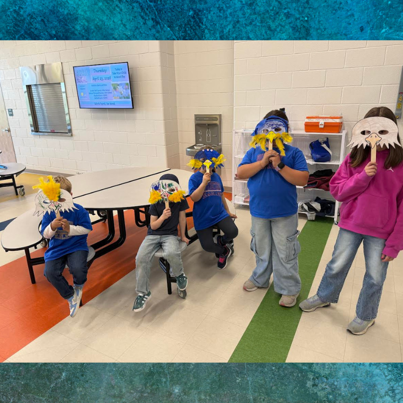 Children in a classroom wear handmade bird masks, some with yellow feather accents.