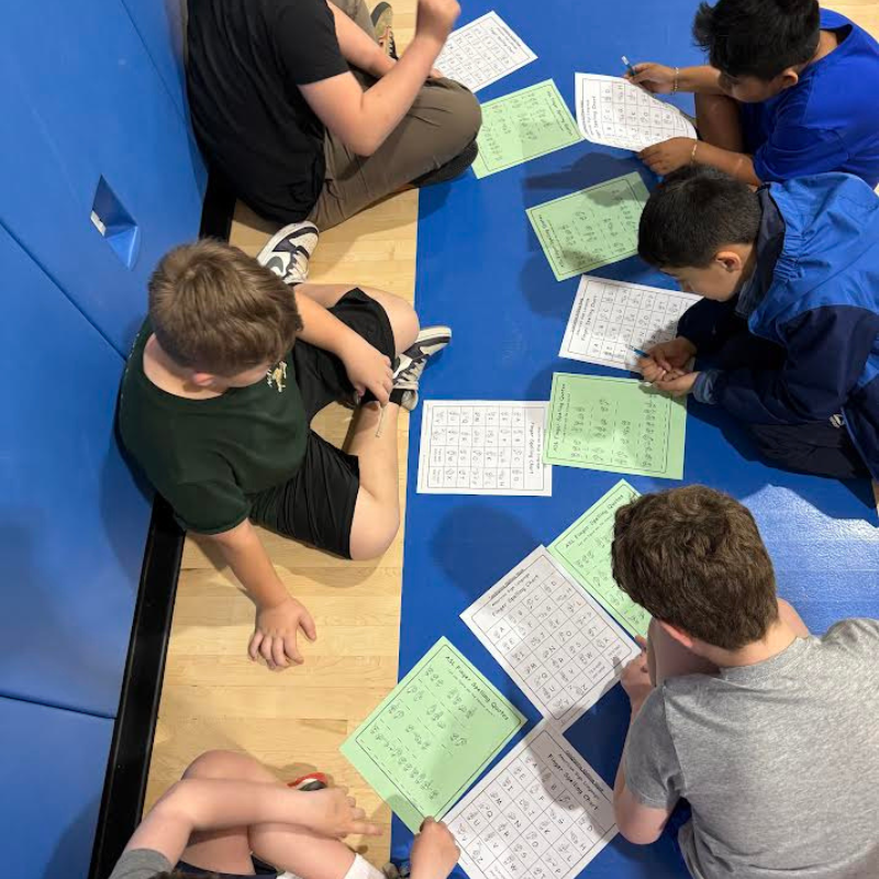 Students sit on the floor, focused on worksheets with charts and text.