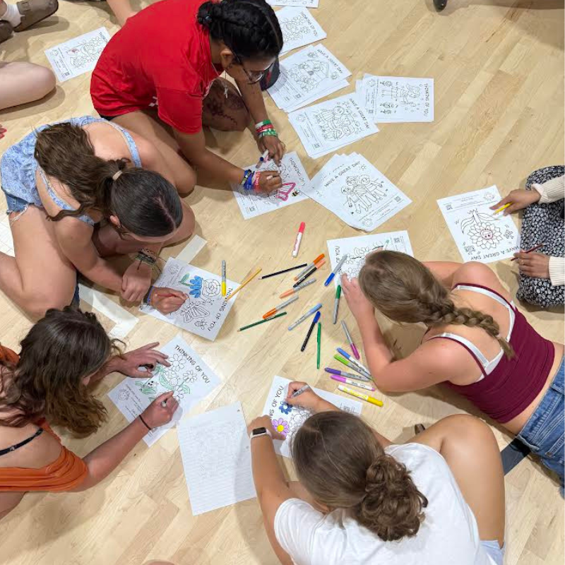 A group of young people are sitting on the floor, coloring pages with markers and pencils.