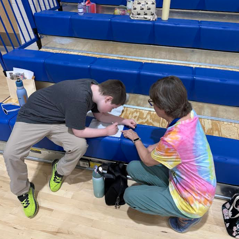 A young person and an adult sit on bleachers, working on a paper together.