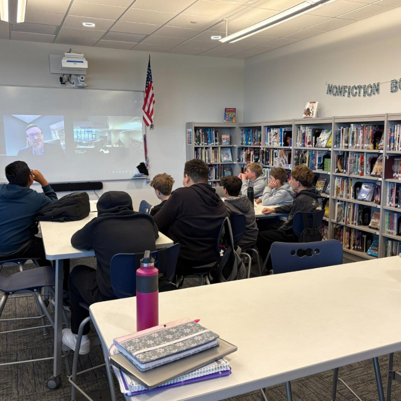 Students watch a video presentation on a projector screen in a library classroom.