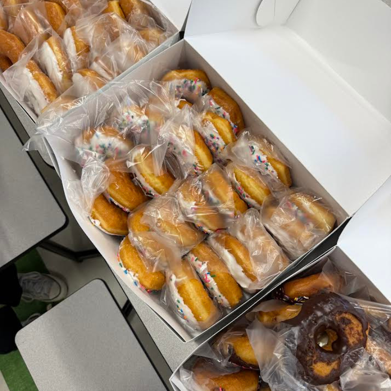 Several white boxes filled with individually wrapped donuts, some with sprinkles.